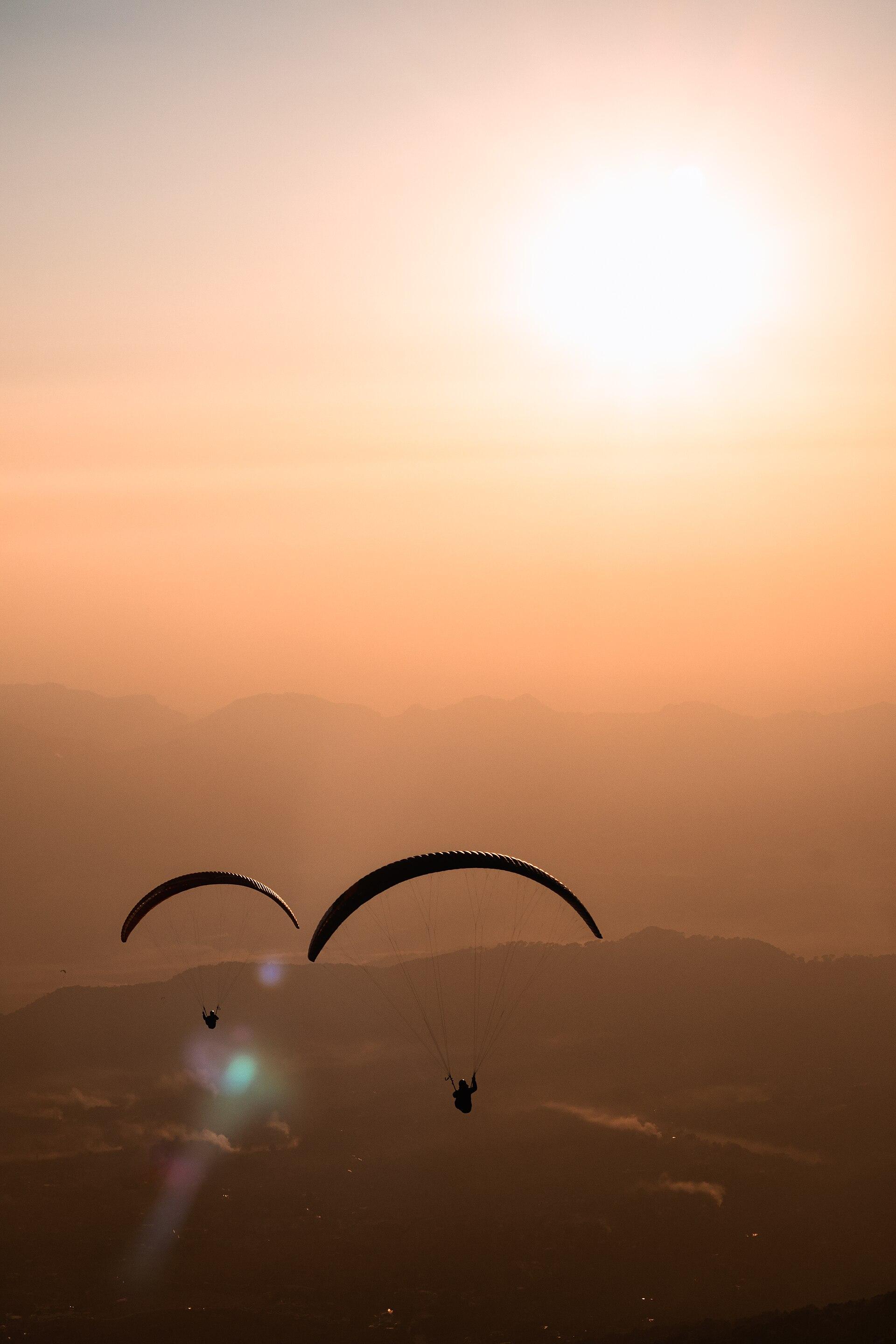 Two paragliders against an orange sunset over Bir
