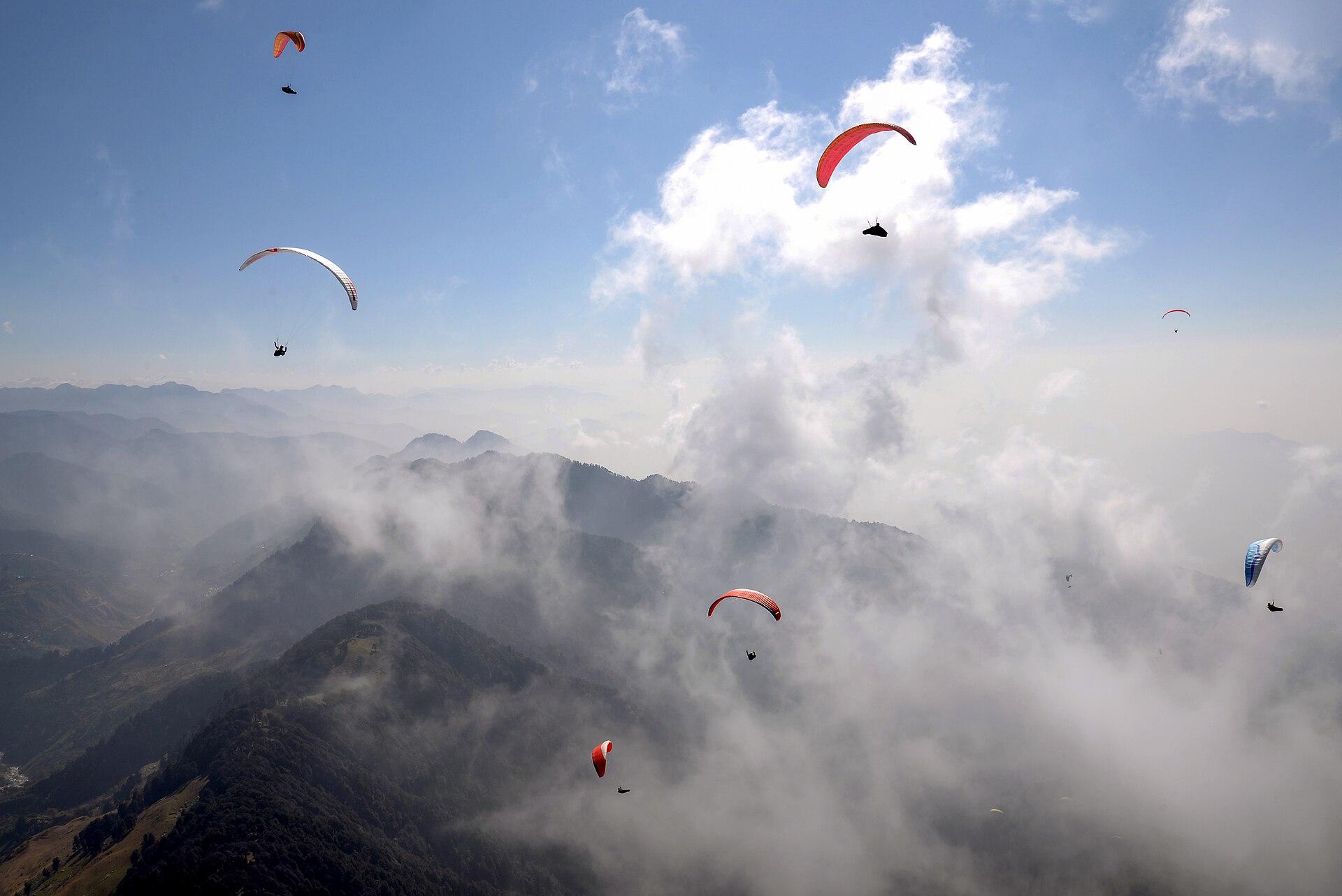 Flying a paraglider high above a valley, the canopy overhead and a field of cloud all around