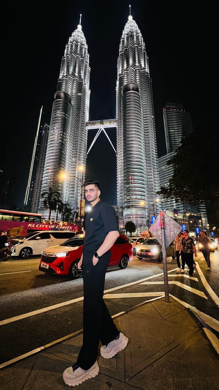 Akshat on a city street at night, the Petronas Towers lit up behind him