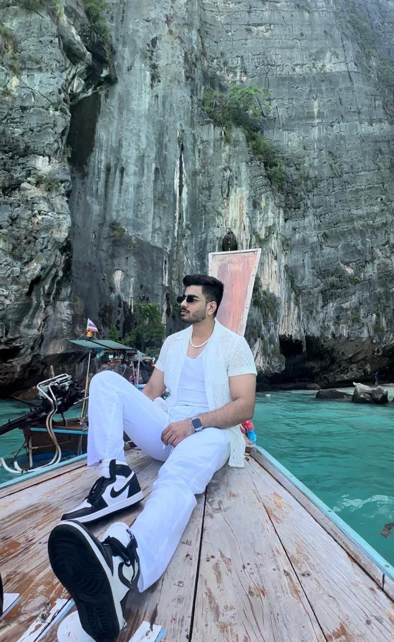 Akshat sitting on the bow of a longtail boat in turquoise water below limestone cliffs
