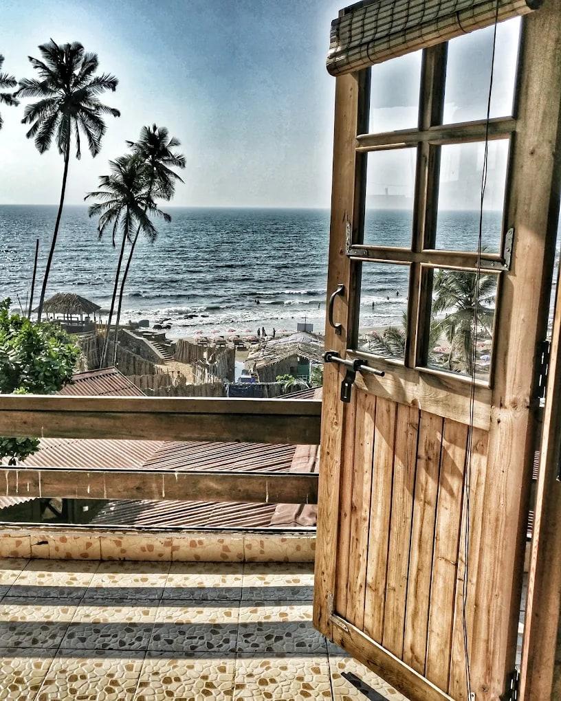An open wooden door onto a balcony, palms and the sea beyond, the beach below