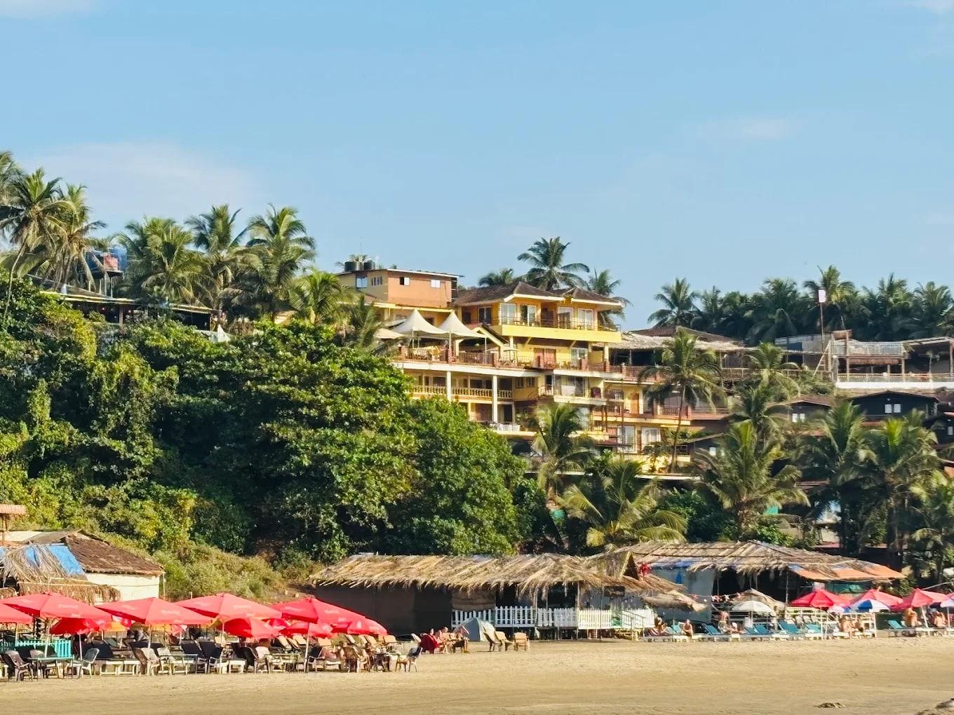 A terraced beachfront guesthouse among palms, seen from the sand with parasols and loungers in front