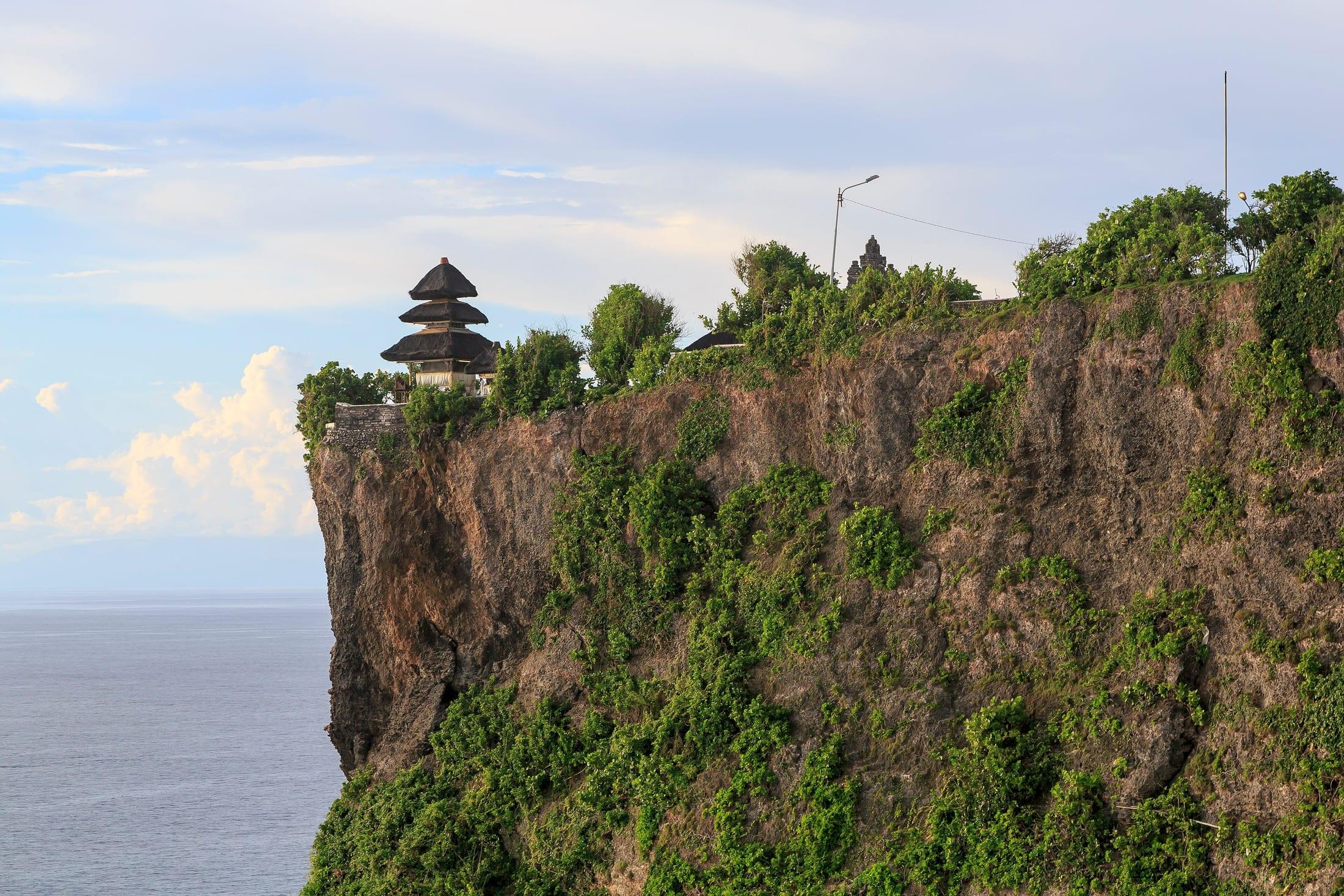 A limestone sea cliff above breaking surf, with a small tiered-roof structure set back on the headland