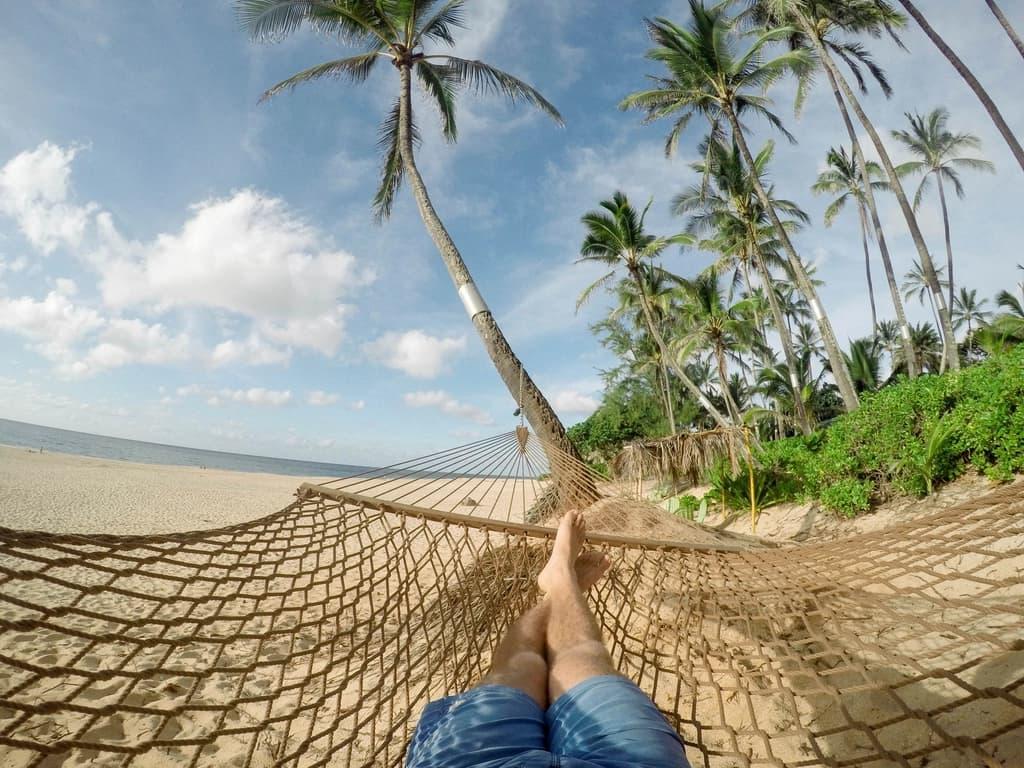 Looking past bare feet in a hammock to palm trees and sea
