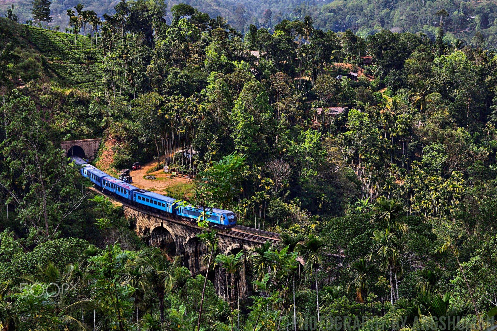 A blue train crossing the stone arches of the Nine Arches Bridge, deep in the jungle