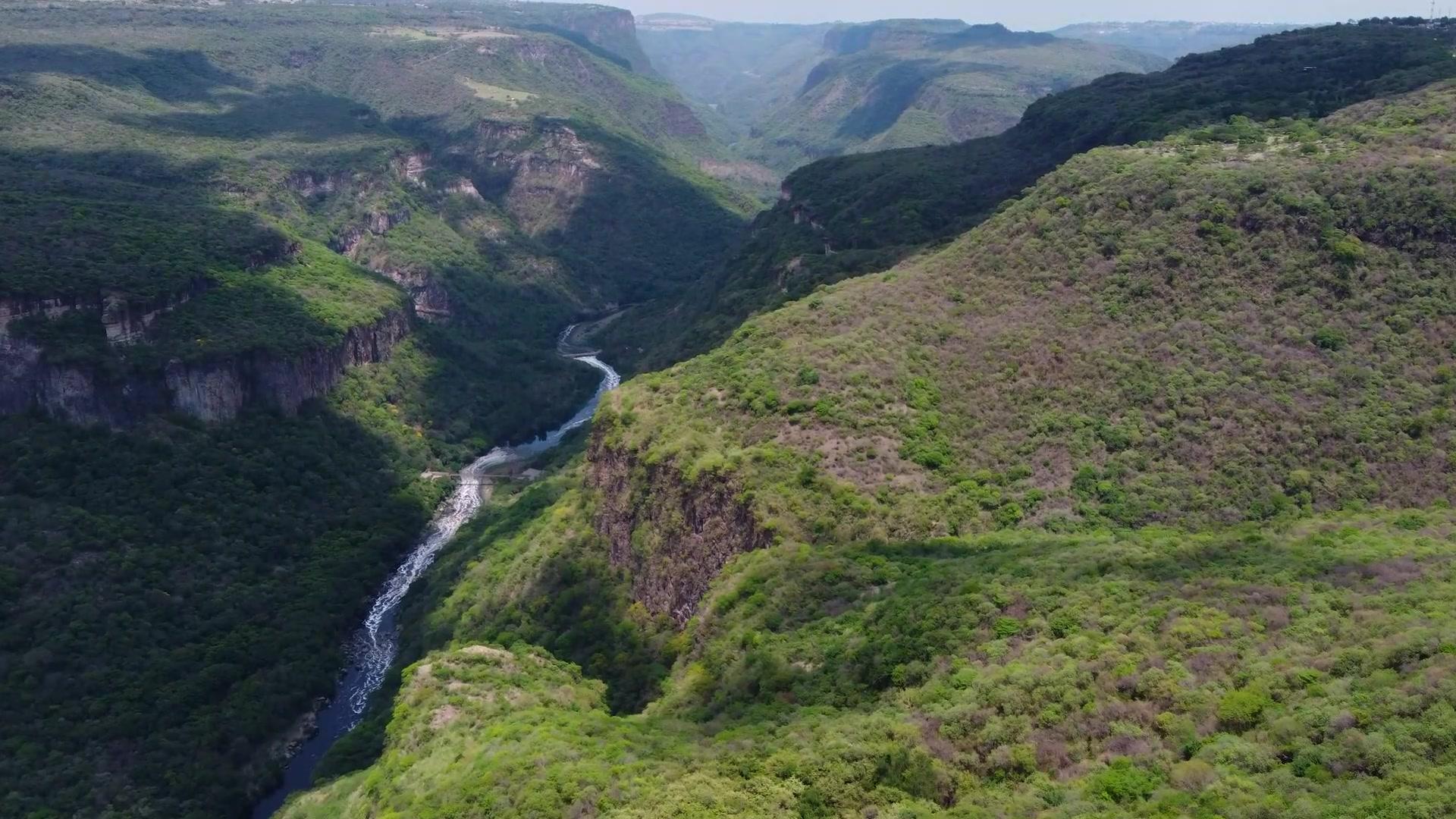 Flying over a deep green valley, a river threading through the bottom of it