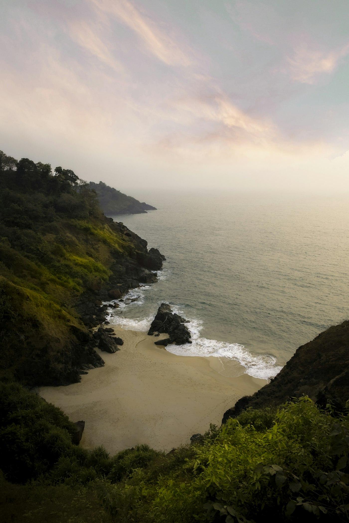 A small cove seen from a clifftop, rocky headlands running out into a hazy sea