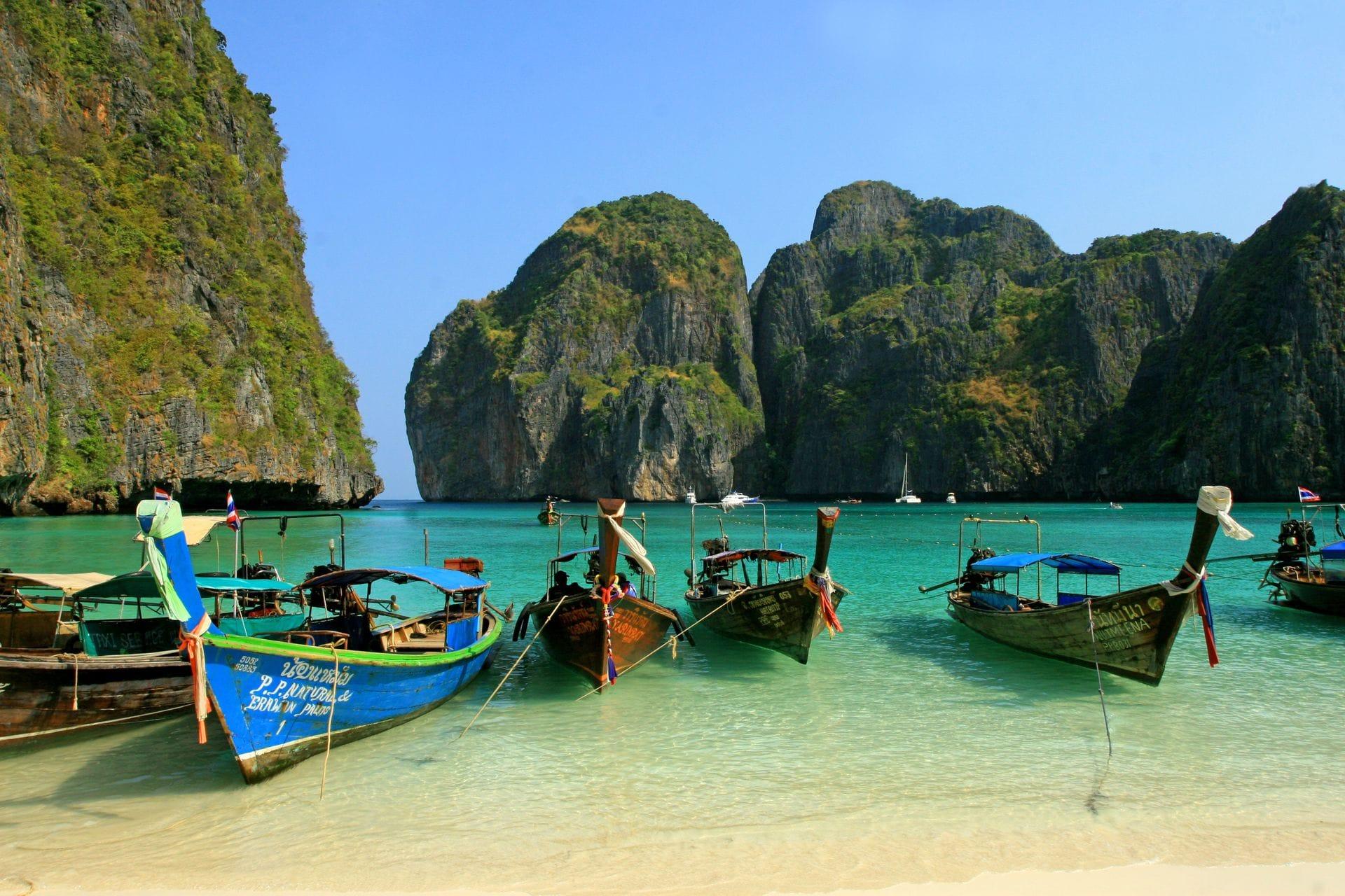 Longtail boats on turquoise water below limestone cliffs